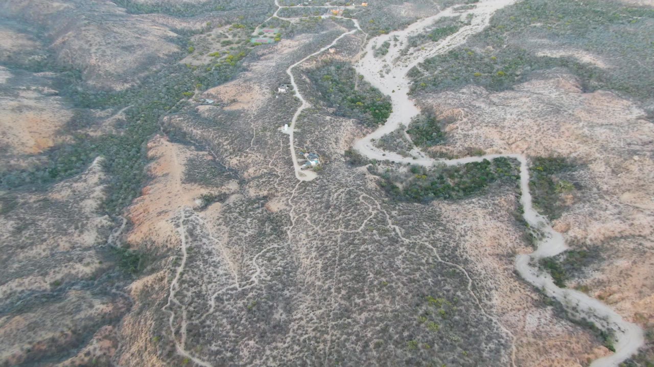Aerial frame over Cabo Pulmo dry hills showing a pale dirt road curving through scrub-covered ridges, with no visible people.