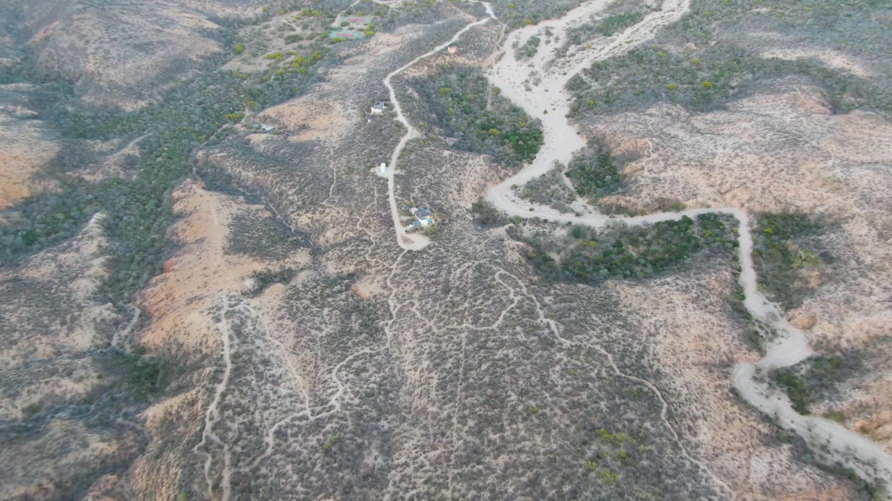 Drone view of a dirt road bending between scrubby ridges and dry washes.