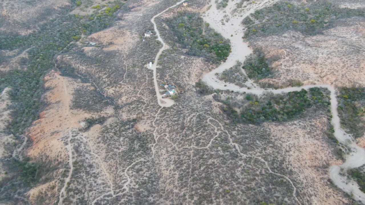 Aerial shot of a dirt road and dry hillside with a small vehicle near the road.