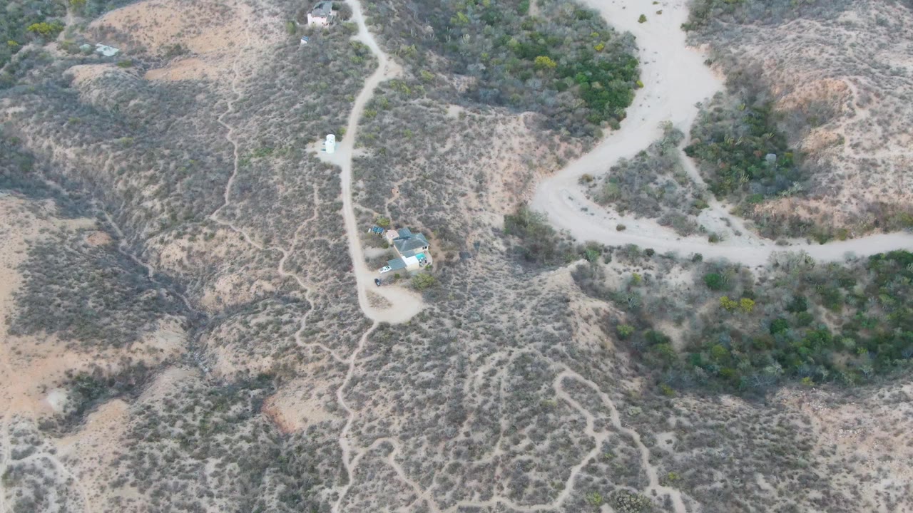 Overhead hillside road scene with a vehicle and sparse desert vegetation.