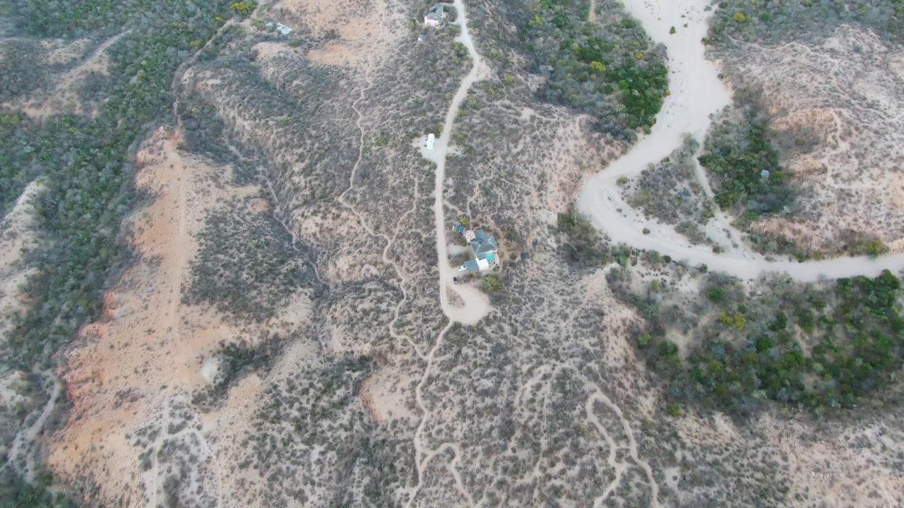 Aerial view in Cabo Pulmo, Baja California Sur, showing a small vehicle on a pale dirt road between scrub-covered hills, with no visible people.
