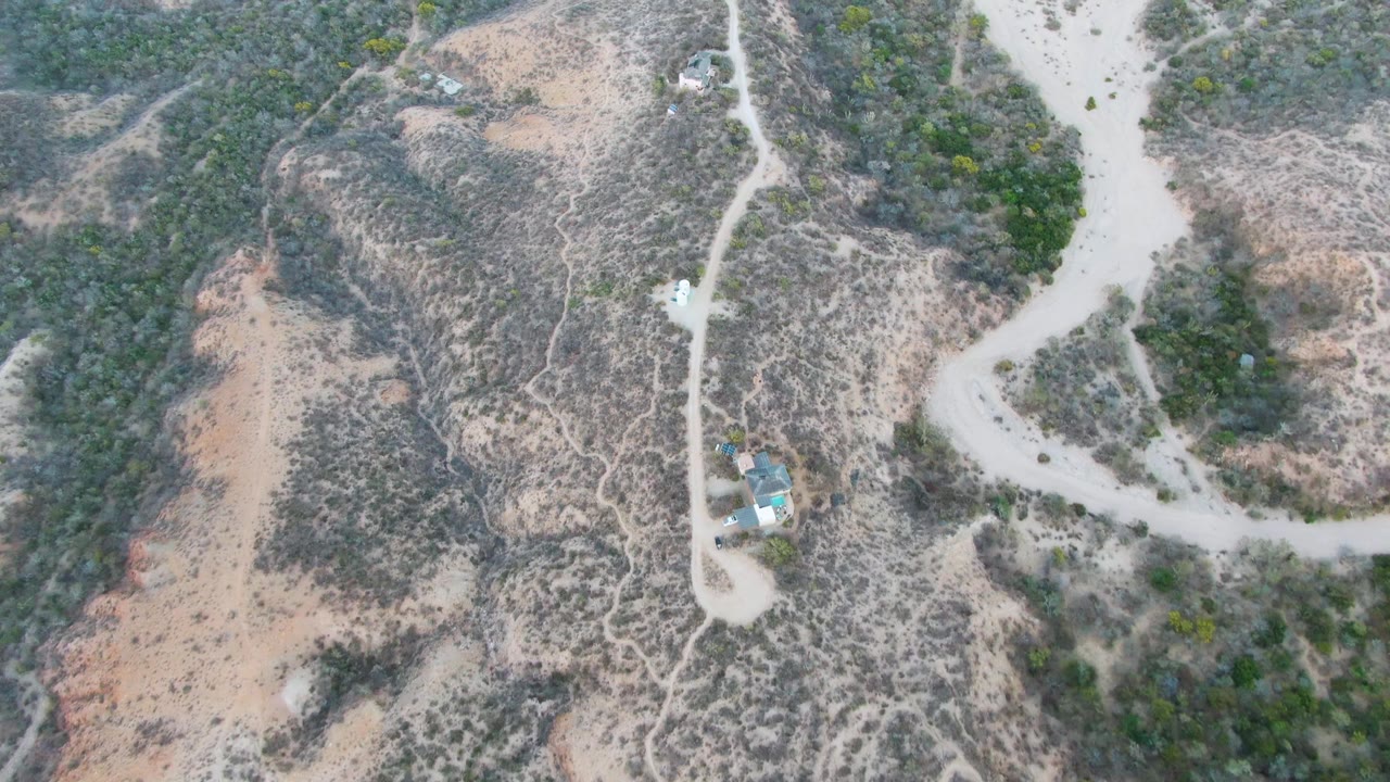 Drone-like view of a dirt road crossing dry hills with a small vehicle visible on the road.