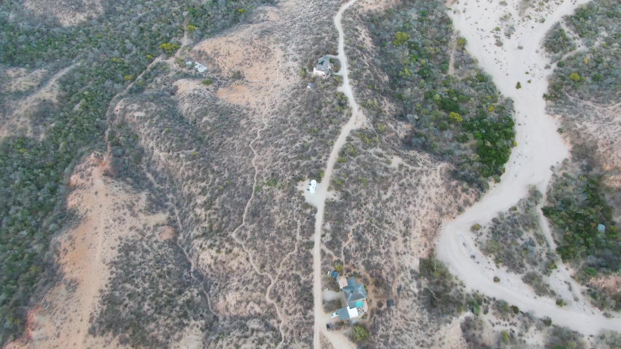 White vehicle on a pale dirt road crossing arid hills with scrub and dry washes.