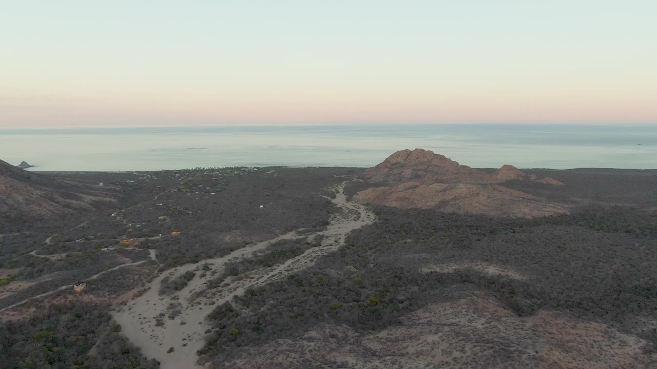 Aerial coastal landscape with dirt road, scrub hills, and calm ocean