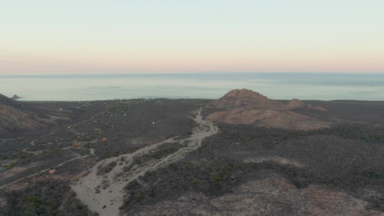 Aerial view of a winding dirt road through coastal hills at dawn