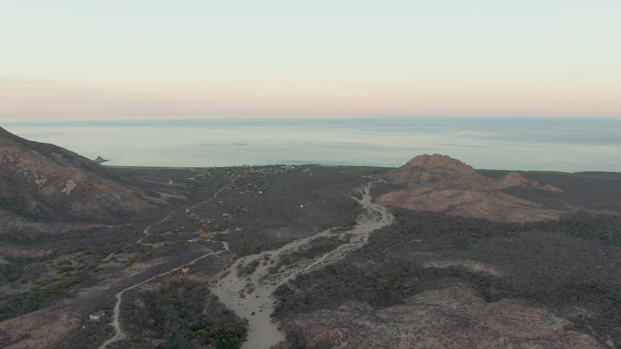 Aerial view of a winding dirt road through dry hills near the ocean.