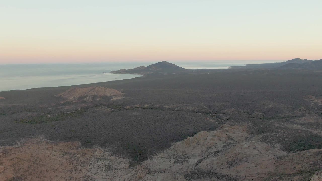 Aerial dusk landscape with rocky foreground, dark terrain, coastline, and ocean.