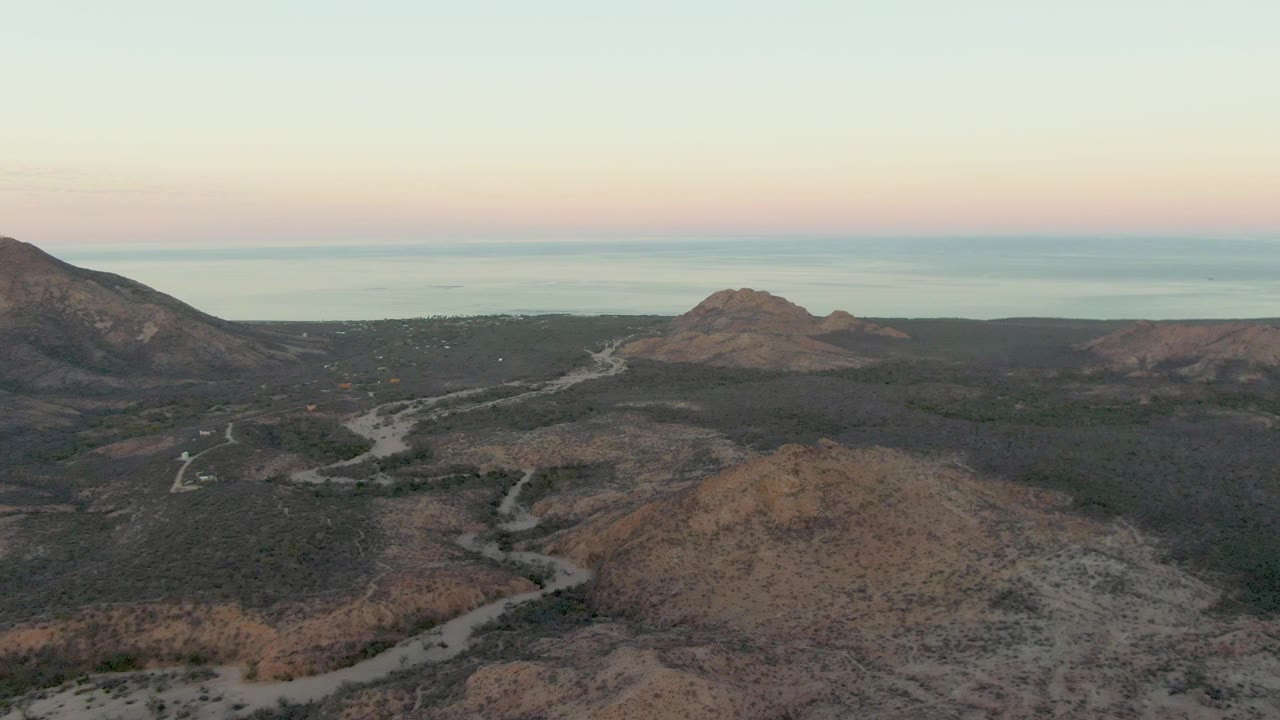 Aerial view of a winding dirt road through arid hills near distant water.