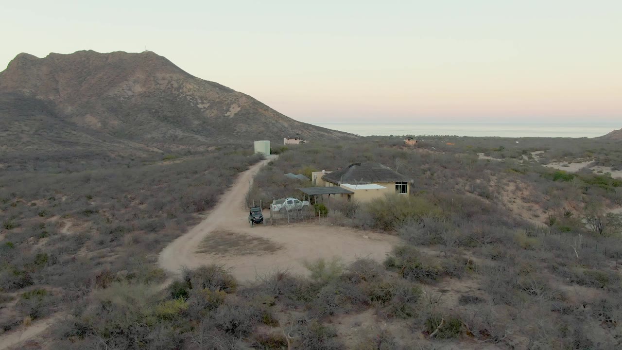 Drone view of a small desert house and parked vehicle beside a winding dirt road.
