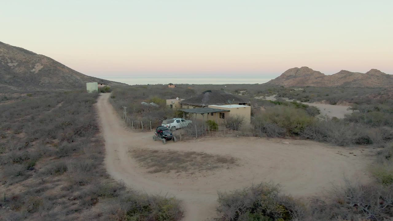 Wide aerial view of a small building and truck beside a winding desert road