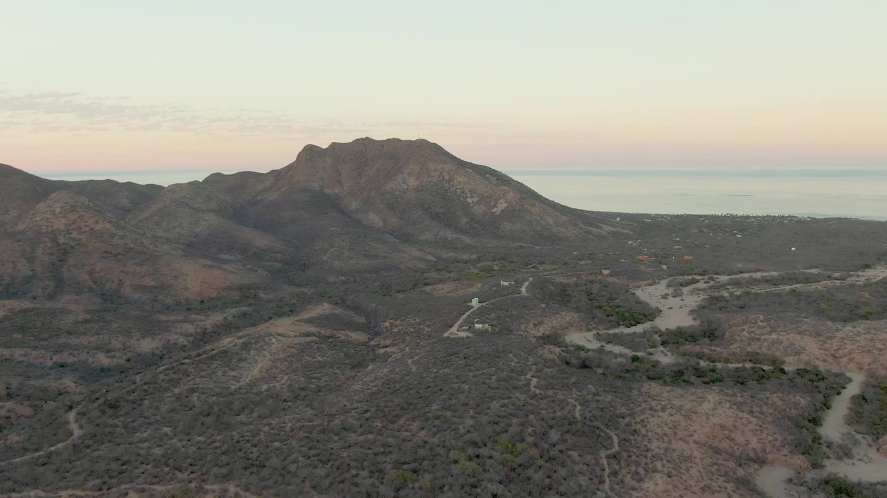 Cabo Pulmo aerial view with rugged mountains to the right, winding dirt roads through dry terrain, ocean on the horizon, and no visible people.