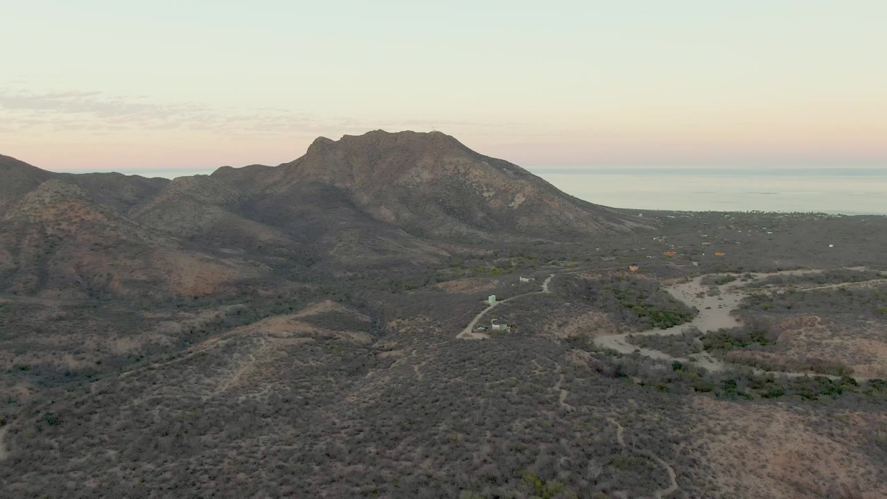 Aerial view of dry hills, a dirt road, mountains, and distant sea