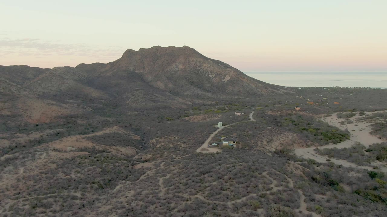 Aerial view in Cabo Pulmo showing the winding dirt road running through scrub-covered hills, with the mountain ridge centered and no visible people.