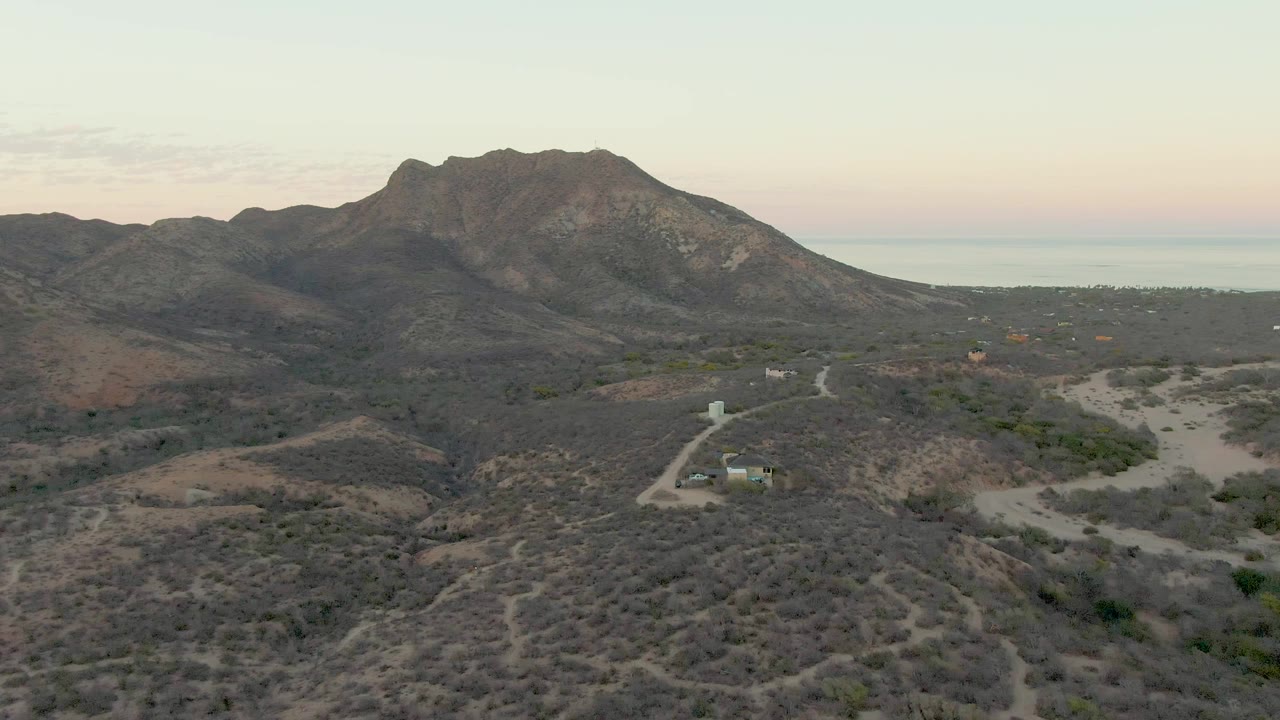 Cabo Pulmo aerial frame with scattered desert buildings near the road, low brush in the foreground, mountains across the horizon, and no visible people.