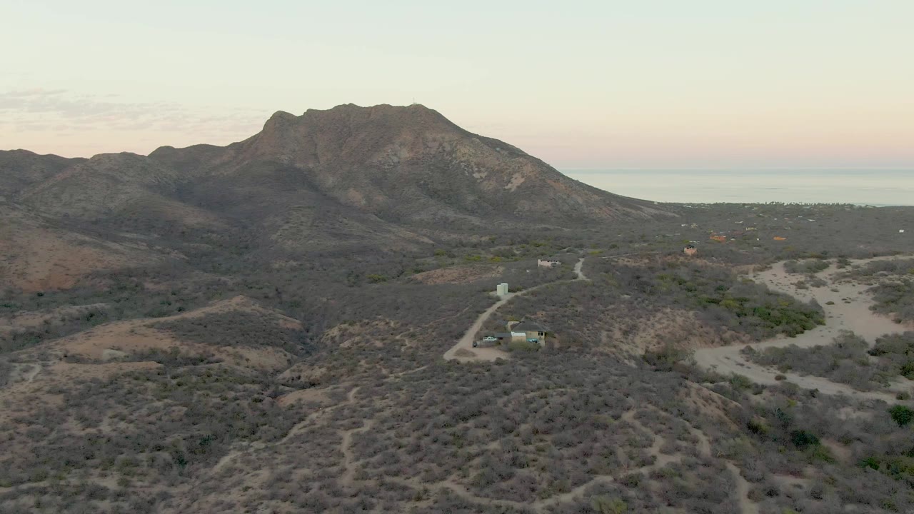 Aerial shot of a vehicle route through scrubby desert hills and mountains.