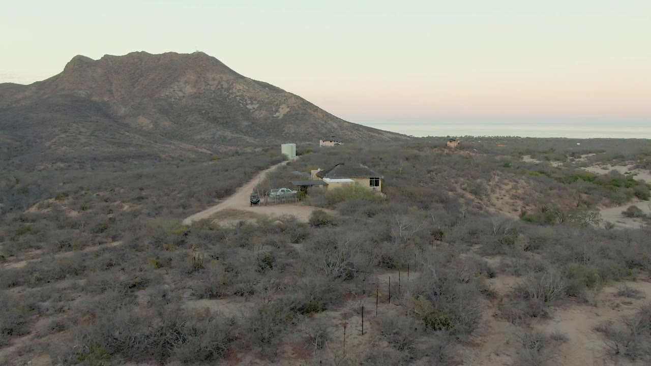 Desert residence with parked vehicle, winding dirt road, scrub, and mountain behind.
