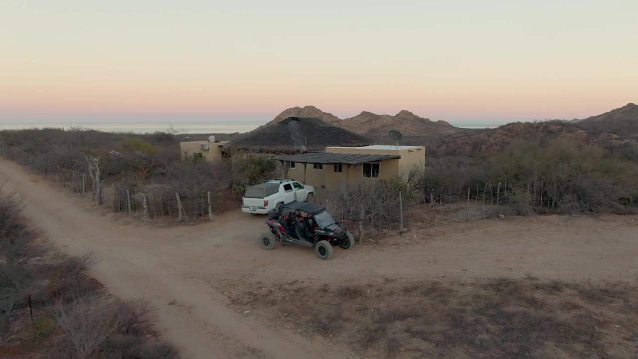 White pickup and ATV by a small house with desert hills in the background.