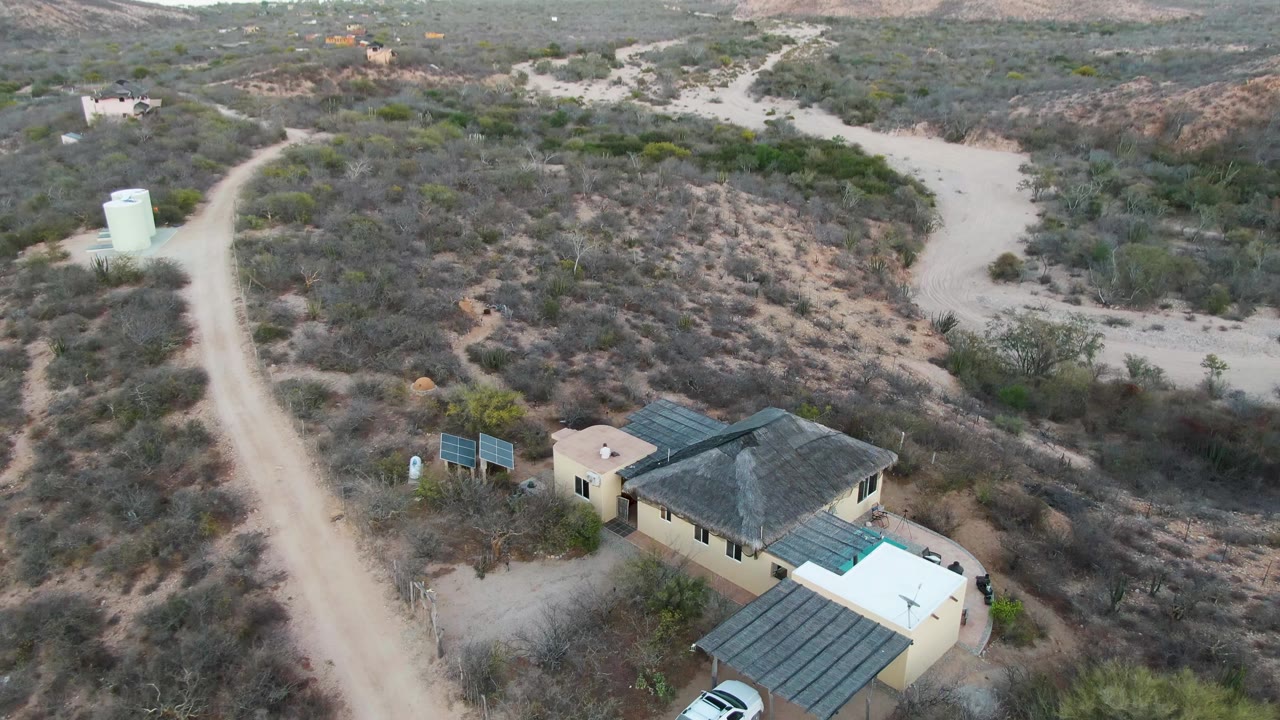 Drone view moving closer to a desert house and dirt road.