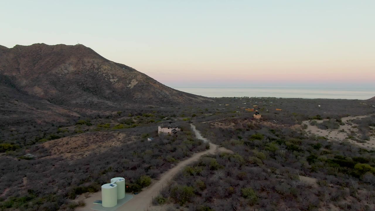 Mountain and coastal horizon over a dry hillside road with tanks at the bottom edge.