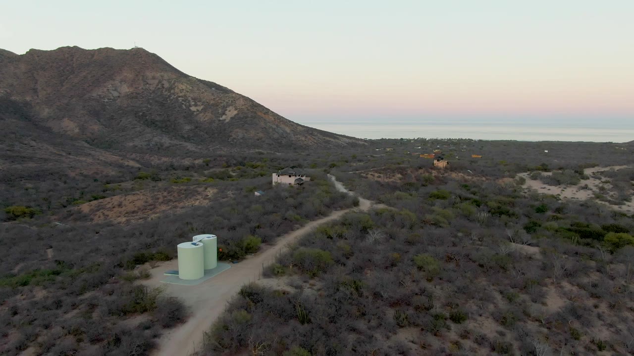 Desert road passing water tanks below mountains