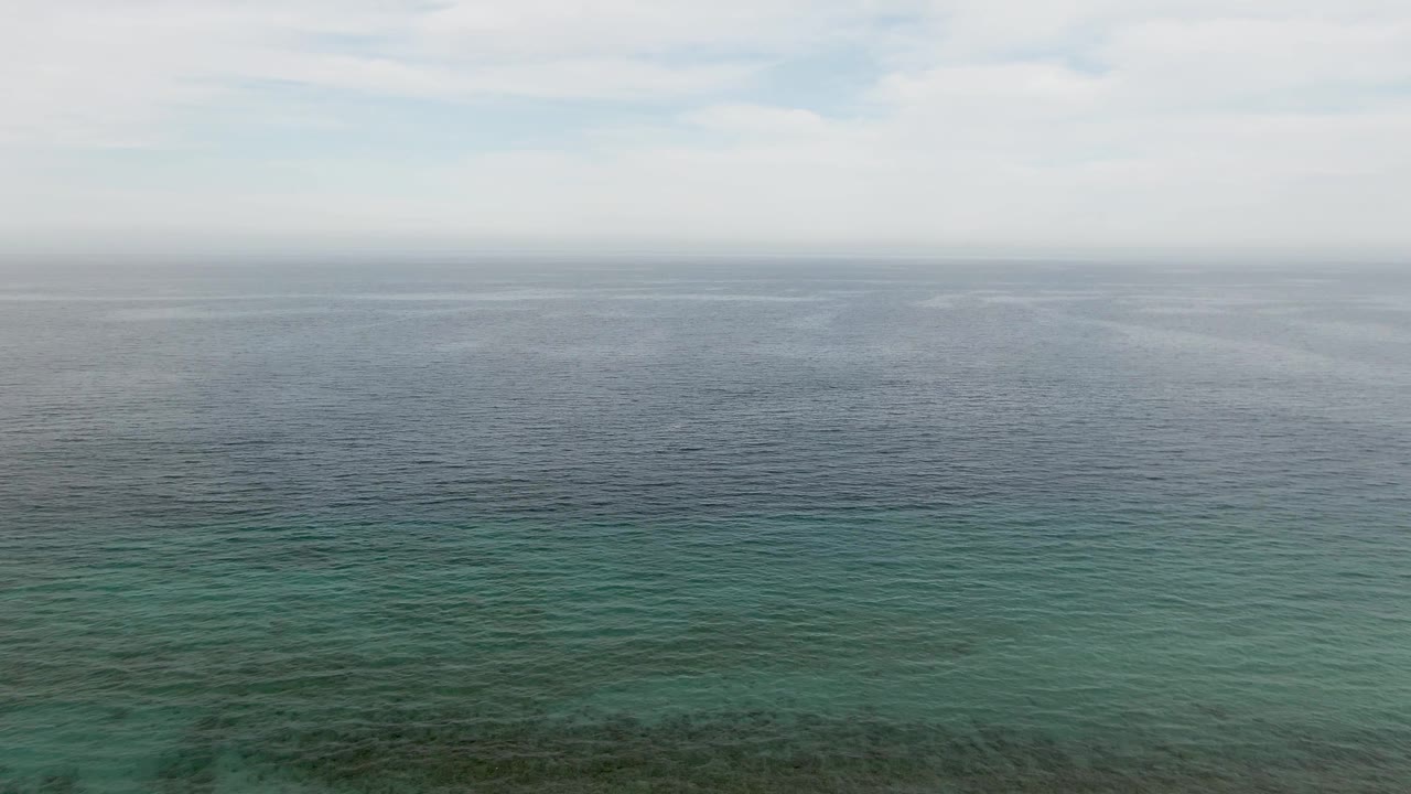 Wide ocean horizon with deep blue water and faint turquoise shallows.