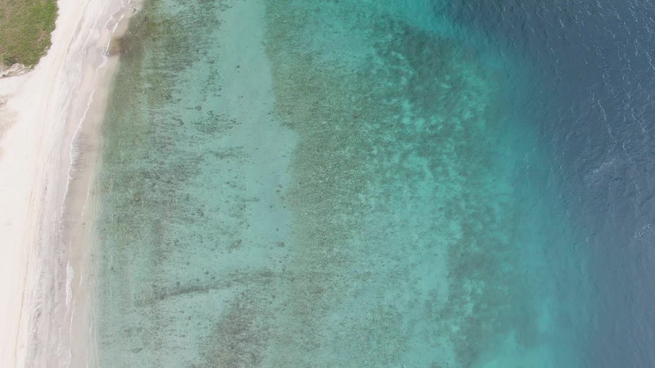 Aerial view of white sand beach beside clear turquoise water.