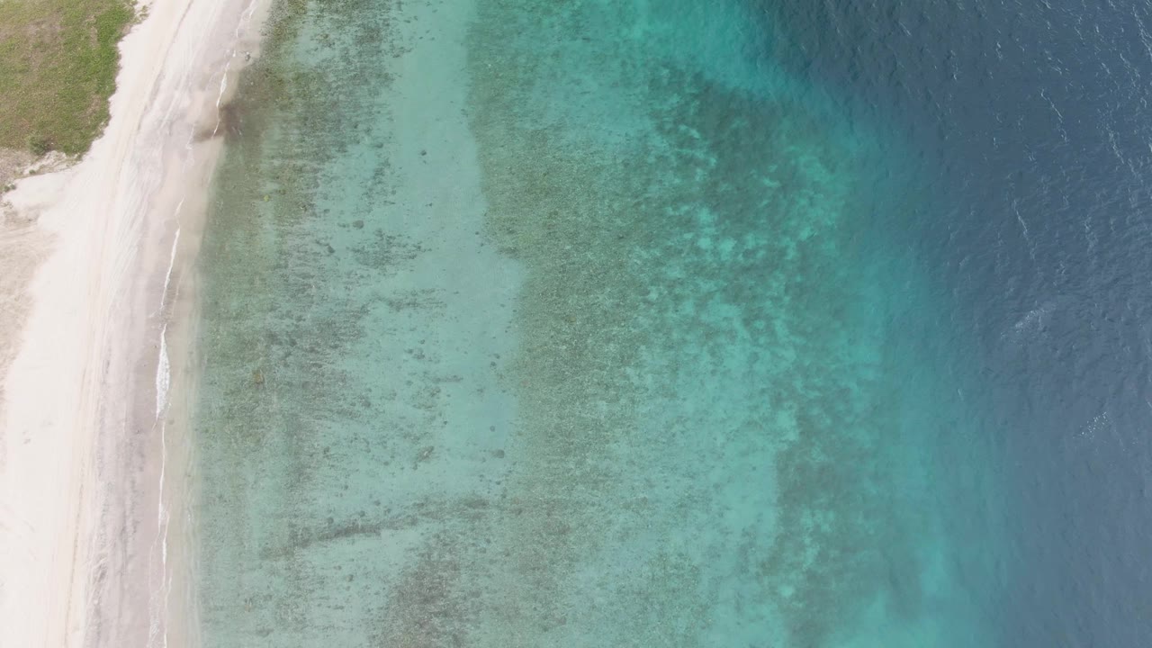 Top-down drone frame from Los Barriles with a narrow strip of white beach on the left, broad clear turquoise shallows across the center, deeper blue sea at right, and no visible people.