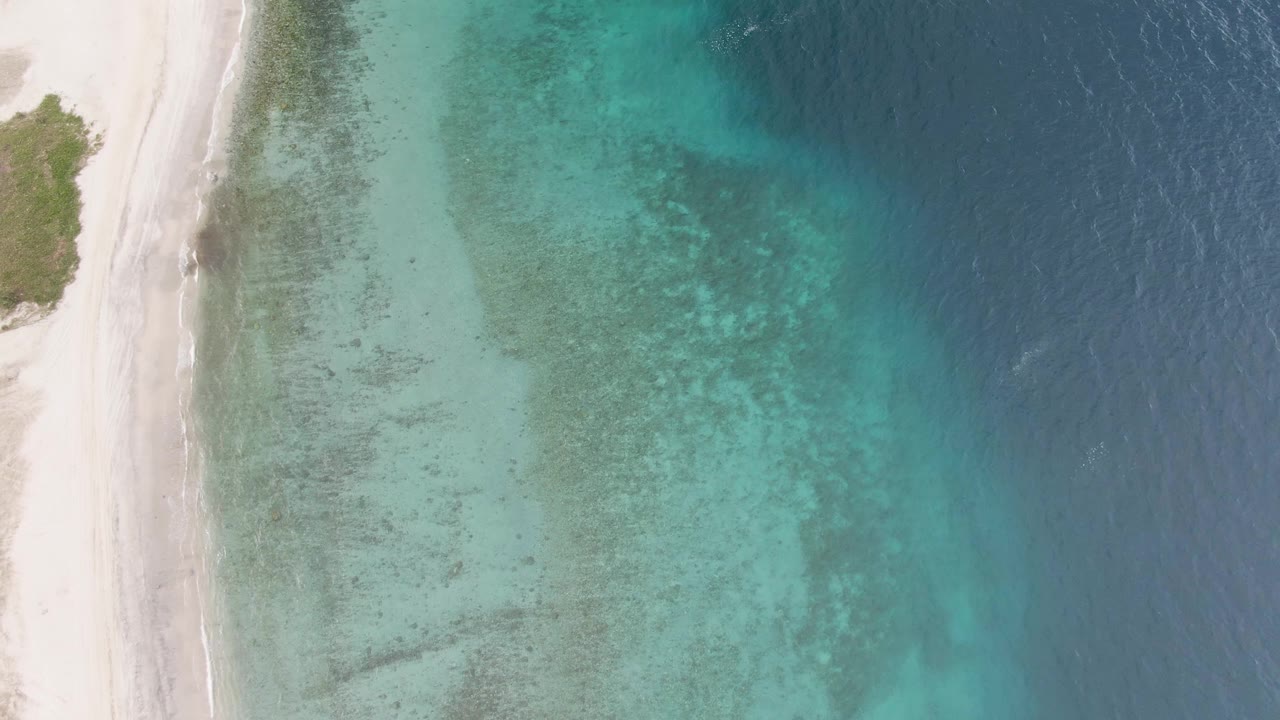 Overhead view of the Los Barriles shoreline at 0:00, with white sand along the left edge, clear turquoise shallows over visible seabed, deeper blue water to the right, and no visible people.