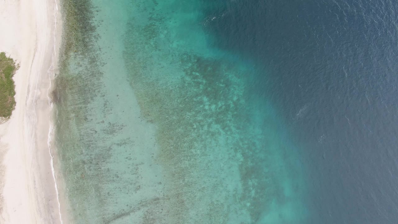 At 0:02, the Los Barriles beach remains tight to the left edge while transparent turquoise water shows mottled seabed patterns before fading into darker blue ocean, with no visible people.