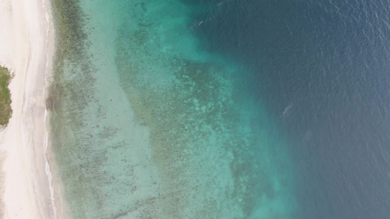 At 0:03, the overhead Los Barriles view shows a slimmer strip of beach at left, a wide field of pale turquoise shallows, darker offshore water at right, and no visible people.
