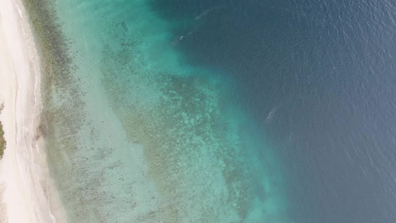 Overhead view of Los Barriles shoreline with white sand on the left, pale turquoise shallows in the center, darker blue ocean on the right, and no visible people.