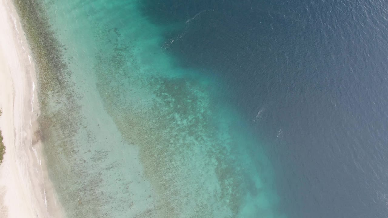 White beach edge beside clear turquoise shallows and dark blue water