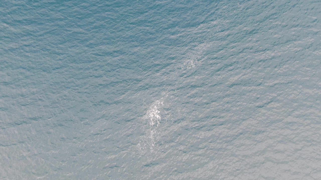 Overhead view of blue-green ocean water near Los Barriles with a small white wake patch near the lower left and no visible people.