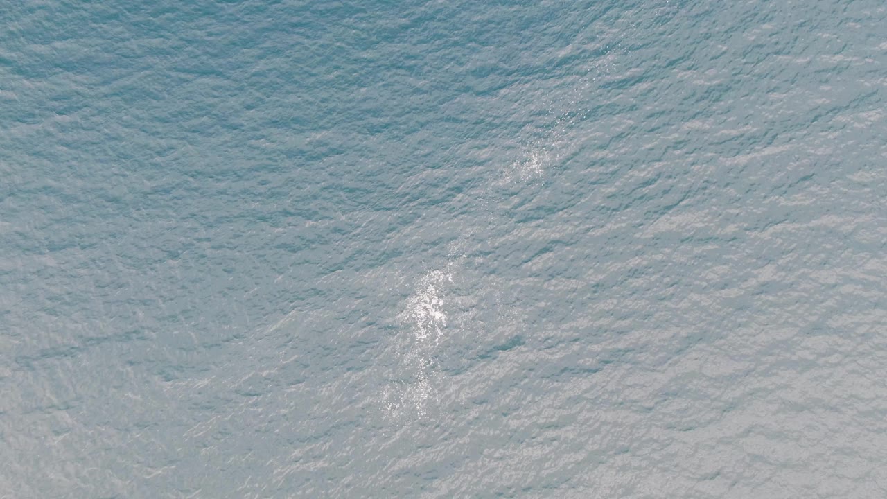 Overhead Los Barriles ocean frame with the white foam wake slightly farther across the rippled blue-green water and no visible people.