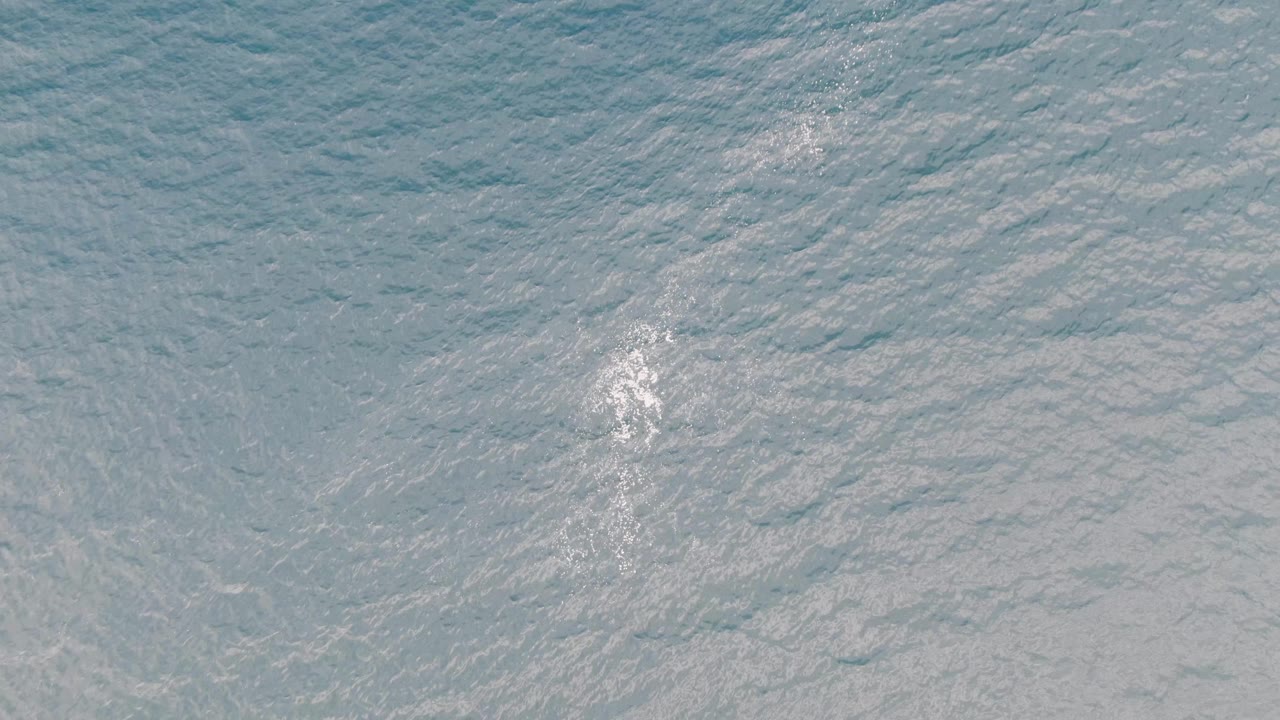 Aerial view of blue-green ocean surface near Los Barriles, Mexico, with a small white foamy wake patch left of center and no visible people.