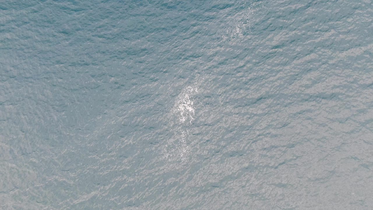 Aerial ocean surface in Los Barriles, Mexico, showing white foam nearer the center of the frame amid fine blue water ripples and no visible people.