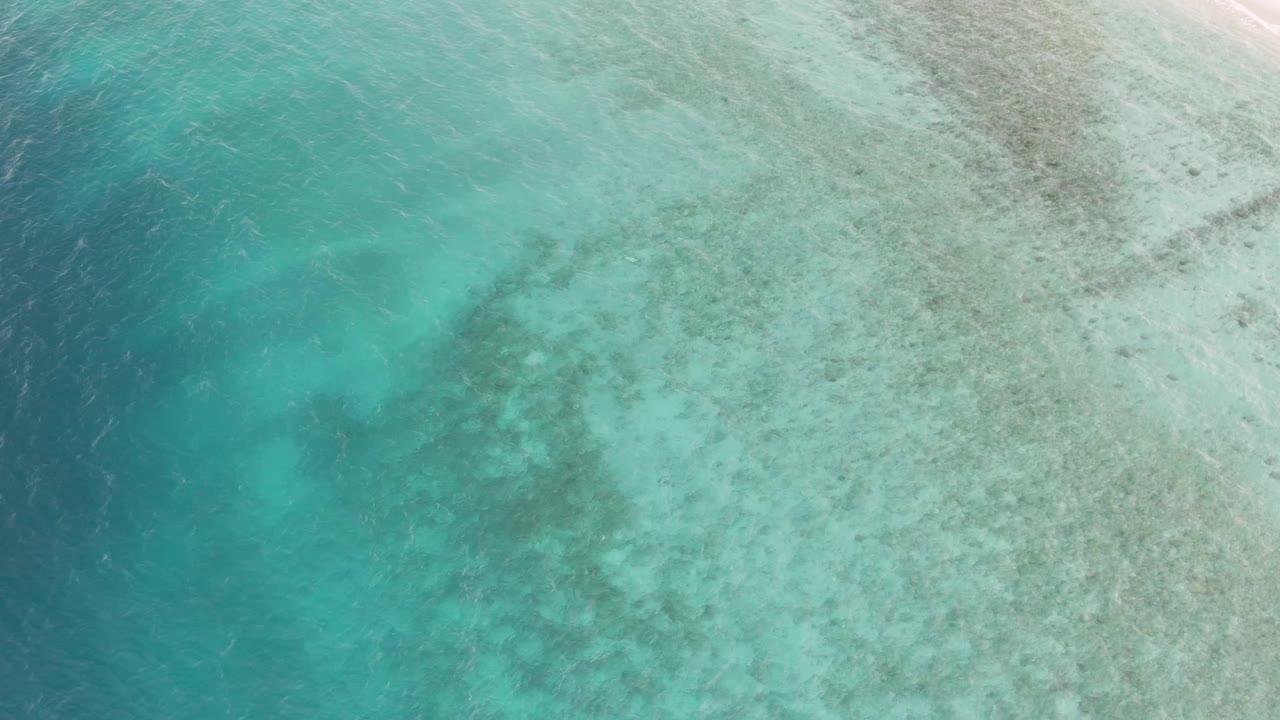 Aerial view of turquoise shallow ocean over a visible seabed near pale sand.