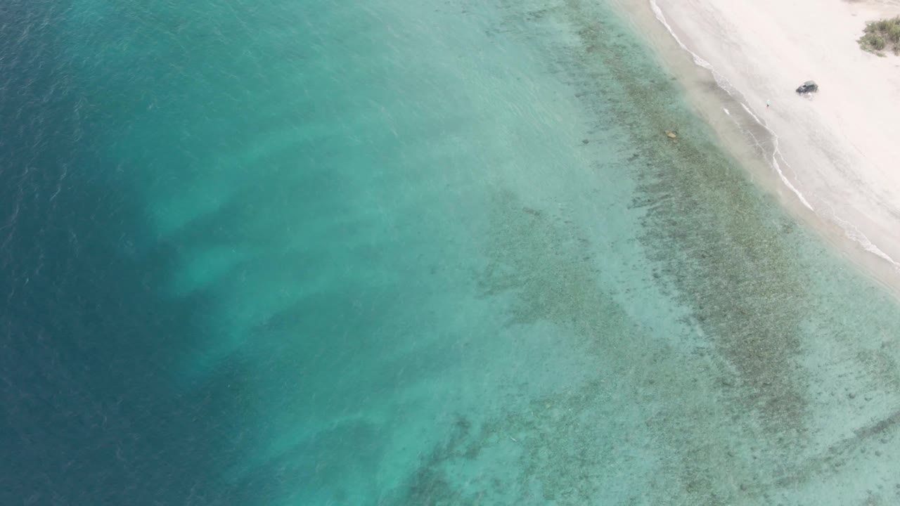 Aerial view of turquoise water beside a sandy beach with a small boat near shore.