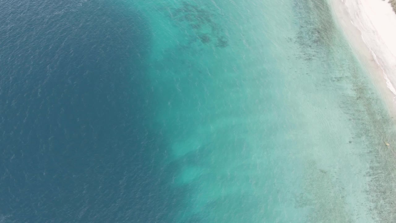 Overhead Los Barriles coastal frame with darker open water on the left, turquoise shallows in the center, and a bright sand strip at the upper right, with no visible people.
