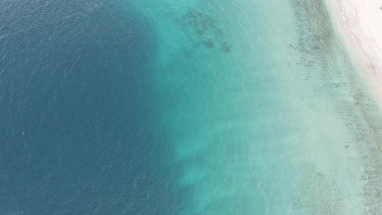 Aerial view in Los Barriles with dark blue water filling the left side, green turquoise shallows across the middle, and white beach at the upper right, with no visible people.