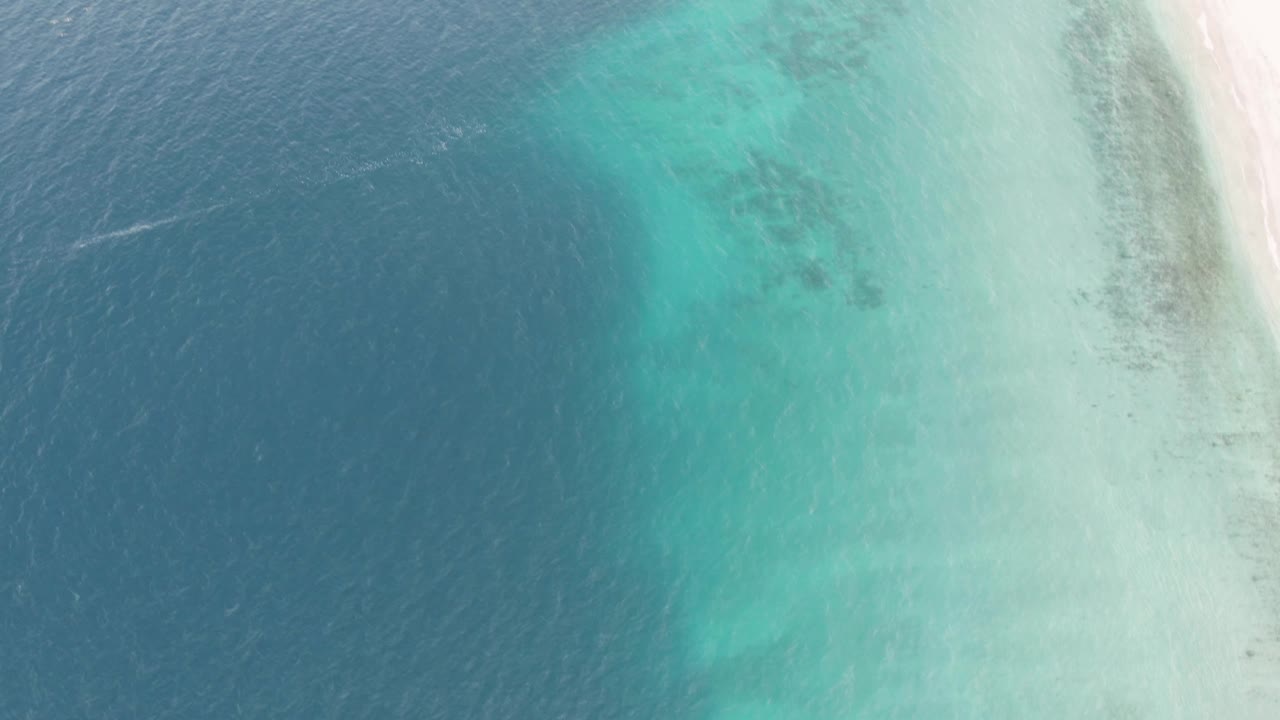 Aerial shoreline with clear turquoise water and darker ocean to the left.