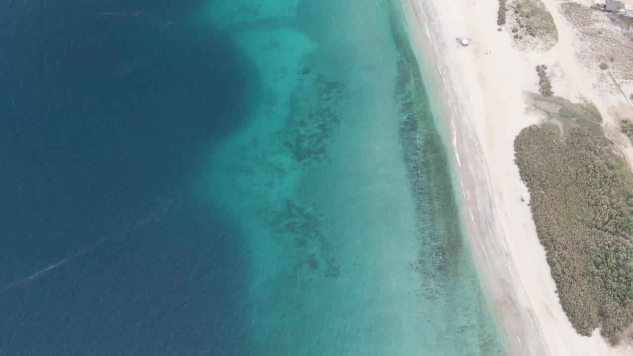 Aerial view of clear ocean water beside a sandy beach road and vegetation.