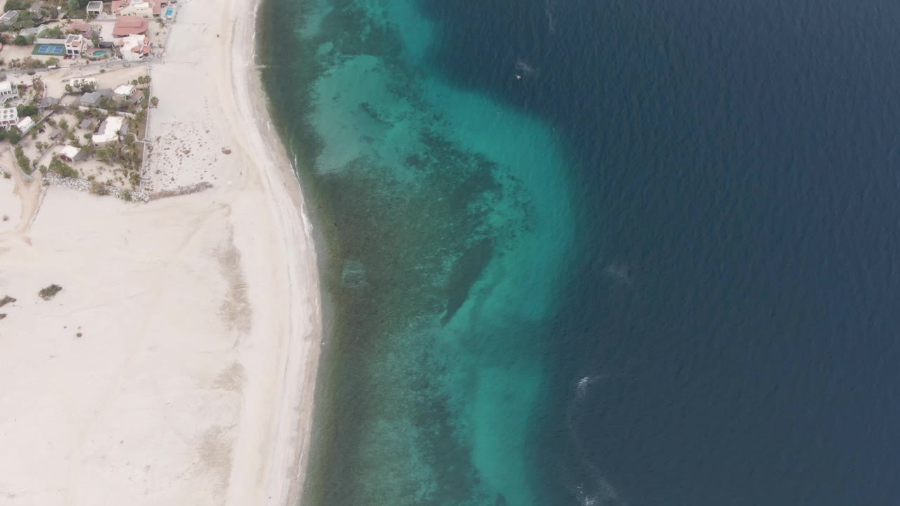 Aerial coastline with broad sand, clear water, and small dark object offshore.