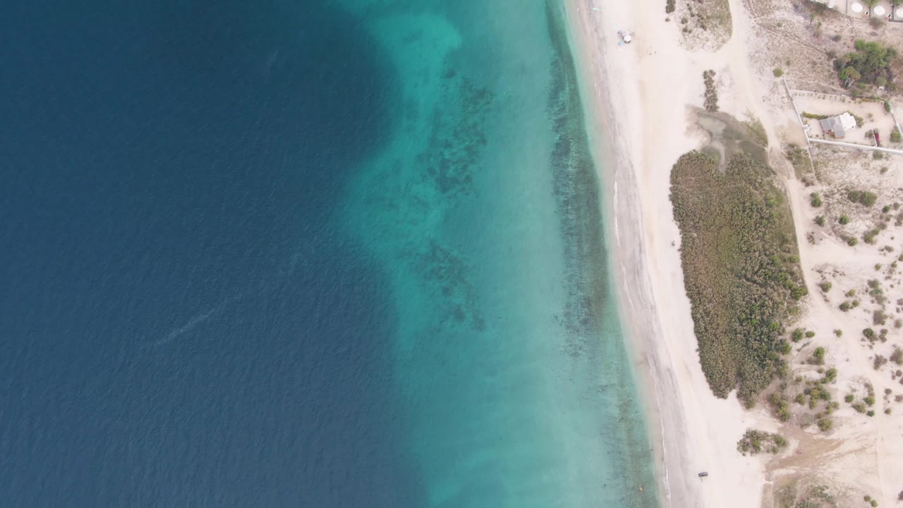 Aerial shoreline with turquoise shallows and sandy road along sparse vegetation