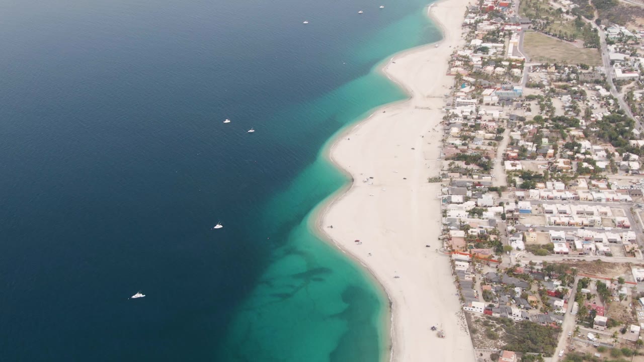 At 0:02 the Los Barriles shoreline remains centered, with several small boats offshore, pale sand below the town edge, and no visible people on the beach.