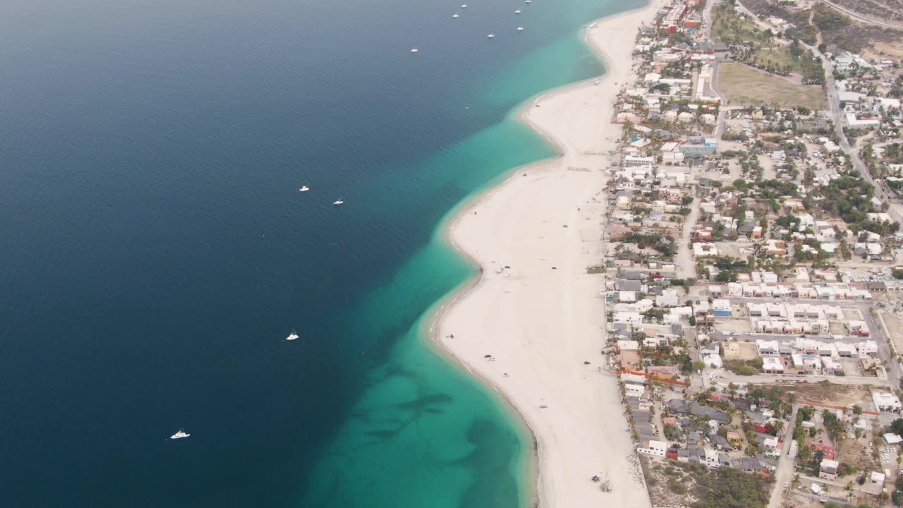 Aerial coastline with dark blue water, bright sand, turquoise edge, and town streets.