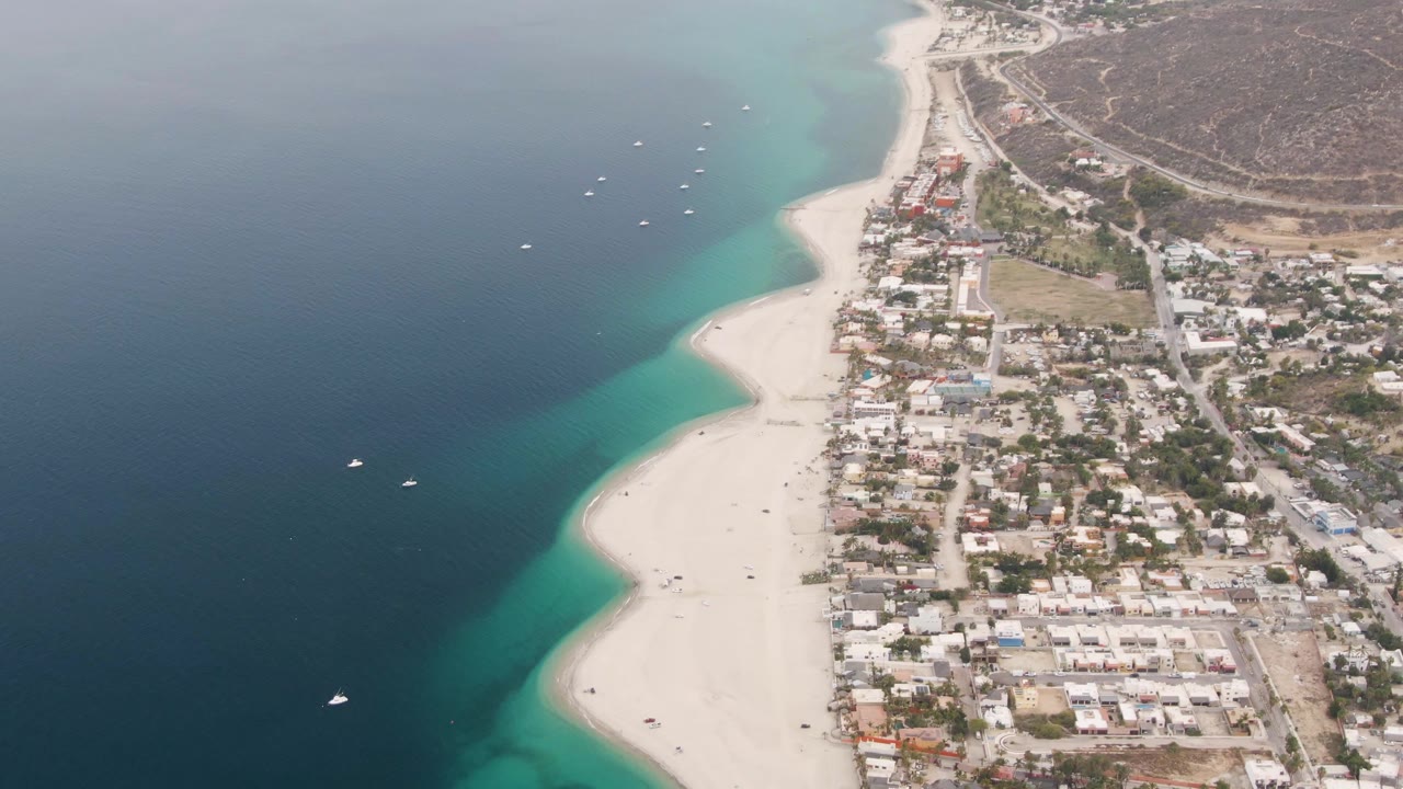 Aerial shoreline with open water, sand, boats, and buildings