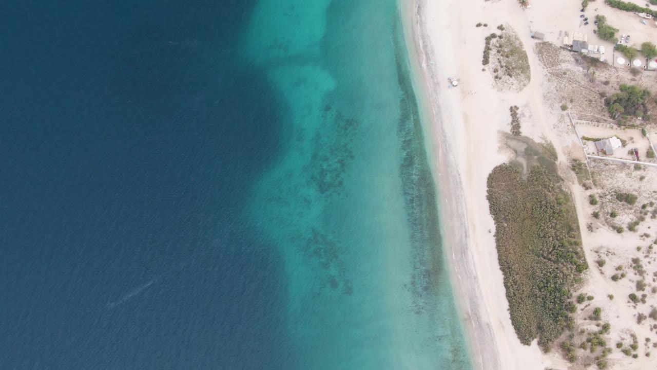 Aerial coastline with clear shallows and a white vehicle on the sand road.