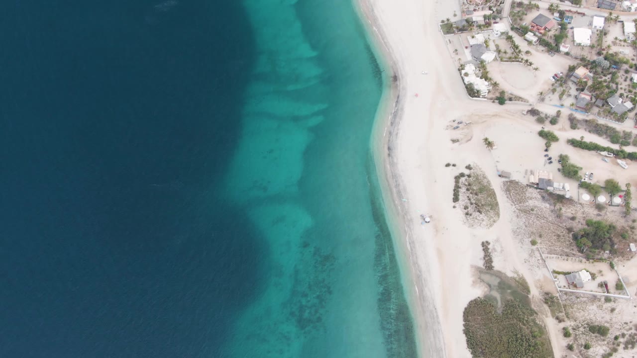 Overhead beach and ocean with turquoise water beside sparse coastal development