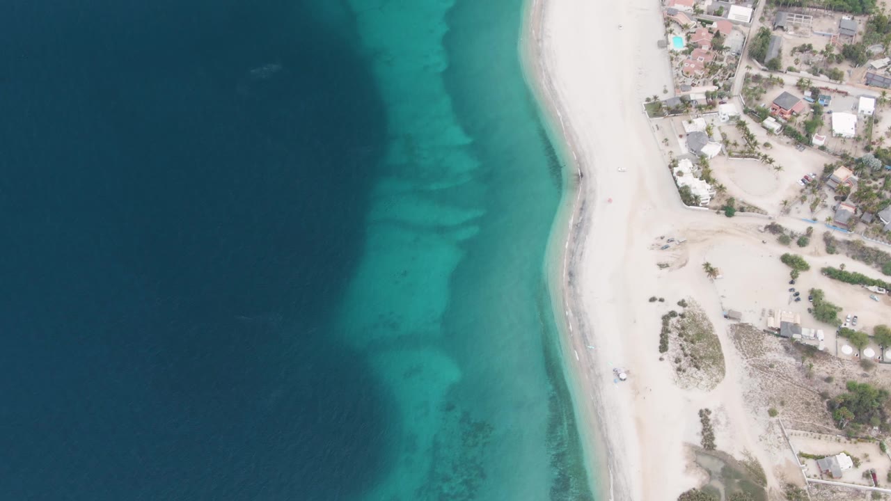 Aerial view of clear water beside a sandy beach and shore buildings.